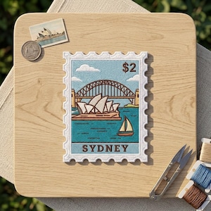 May include: A rectangular embroidered patch shaped like a postage stamp featuring the Sydney Harbour Bridge and Opera House in brown and blue threads. The text $2 and SYDNEY is stitched in brown. The patch has a white scalloped border edge.