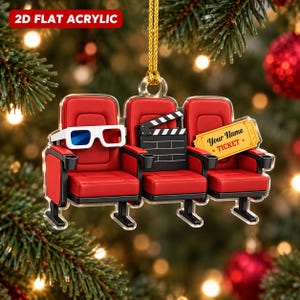 May include: A 2D flat acrylic hanging ornament featuring three red theater seats. The left seat has white 3D glasses, the center seat holds a black film clapperboard, and the right seat displays a yellow ticket with the text Your Name TICKET.