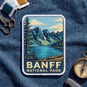 May include: A rectangular embroidered patch featuring a landscape of Banff National Park with mountains, a lake, and evergreen trees. The text BANFF NATIONAL PARK is stitched in cream at the bottom. The patch has a white border and blue background.