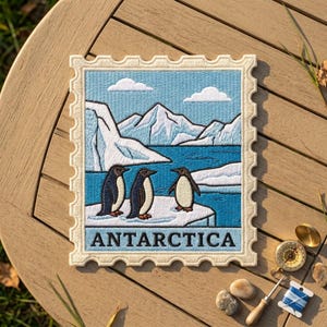 May include: A rectangular embroidered patch shaped like a postage stamp featuring three penguins standing on an ice floe against a backdrop of blue water, white glaciers, and two clouds. The word ANTARCTICA is stitched in black at the bottom.
