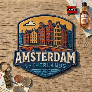 May include: A decorative embroidered patch featuring a colorful illustration of Amsterdam canal houses and a bridge, with the text AMSTERDAM NETHERLANDS. The patch is surrounded by a small flag pin, a miniature bottle of Stroopwafel liqueur, and coins.