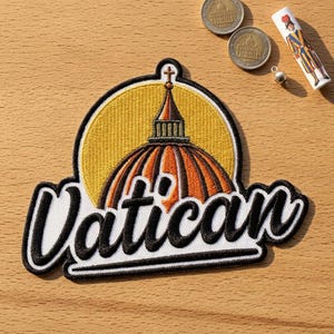 May include: An embroidered patch featuring a yellow circular background with a brown and orange dome topped by a cross. The word Vatican is stitched in large black cursive letters with a white outline across the bottom of the patch design.