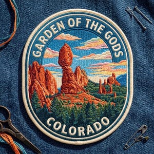 May include: A circular embroidered patch featuring a landscape of red rock formations and green pine trees under a sunset sky. The text GARDEN OF THE GODS is arched at the top, and COLORADO is printed at the bottom in white lettering.