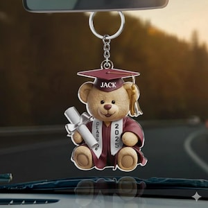 May include: A graduation-themed car charm featuring a teddy bear wearing a maroon graduation cap and gown. The bear holds a diploma and has the name "JACK" on the cap. The year "2025" is displayed on the gown.