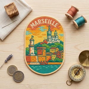 May include: An oval embroidered patch featuring a colorful landscape of Marseille with the text MARSEILLE at the top. The design includes a lighthouse, a church, and buildings in shades of yellow, orange, green, and blue, surrounded by sewing supplies.