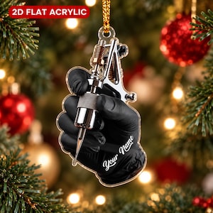 May include: A 2D flat acrylic Christmas ornament featuring a hand wearing a black glove holding a silver tattoo machine. The ornament includes a gold hanging cord and the text Your Name in white script lettering against a clear acrylic base.
