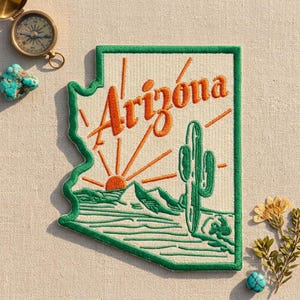 May include: An embroidered patch shaped like the state of Arizona with a green border. The design features an orange sun rising over green mountains and a saguaro cactus, with the word Arizona stitched in orange cursive script across the top.