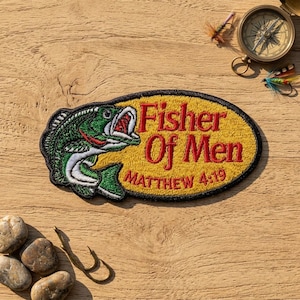 May include: An oval embroidered patch featuring a green and white fish on the left and the red text Fisher Of Men MATTHEW 4:19 on a yellow background. The patch is bordered in black and surrounded by fishing gear including a compass and hooks.