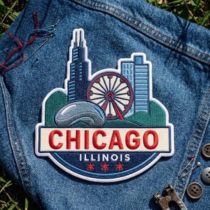 May include: An embroidered patch featuring the Chicago skyline, including the Willis Tower, a Ferris wheel, and the Cloud Gate sculpture. The patch has a cream-colored banner with the red text CHICAGO and the blue text ILLINOIS with three red stars.