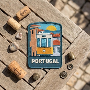 May include: A rectangular embroidered patch featuring a yellow tram traveling through a city with orange-roofed buildings under a yellow sun. The word PORTUGAL is stitched in white capital letters at the bottom against a dark blue background.