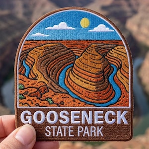 May include: An embroidered patch featuring a landscape of Gooseneck State Park with a winding blue river cutting through orange and brown canyon rock formations under a bright blue sky with a yellow sun and white clouds, with the text GOOSENECK STATE PARK.