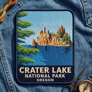 May include: A rectangular embroidered patch featuring a landscape of Crater Lake National Park in Oregon. The design shows a blue lake, golden rock formations, and green pine branches. The text reads CRATER LAKE NATIONAL PARK OREGON.