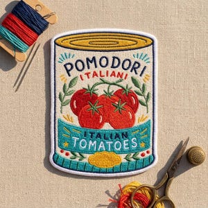 May include: A rectangular embroidered patch featuring a stylized can of tomatoes with the text POMODORI ITALIANI and ITALIAN TOMATOES. The design includes red tomatoes, green leaves, and yellow accents on a white background with a thick white border.