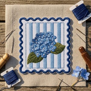 May include: A rectangular fabric patch with a scalloped dark blue border featuring an embroidered blue hydrangea flower with green leaves on a light blue and white striped background, surrounded by sewing needles and blue embroidery thread.