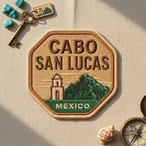 May include: An octagonal embroidered patch featuring the text CABO SAN LUCAS and MEXICO, with a depiction of a building and a mountain. The patch is accompanied by a metal key, turquoise stones, a small matching tag, and a compass.