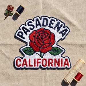 May include: An embroidered patch featuring a red rose with green leaves on a white background. The word PASADENA is stitched in dark blue above the rose, and the word CALIFORNIA is stitched in red below the rose. A small rose pin and thread spools.