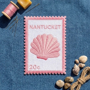 May include: A rectangular embroidered patch shaped like a postage stamp with a pink scalloped border, a white background, a pink seashell illustration, the text NANTUCKET, and the text 20c, accompanied by sewing supplies and seashells.
