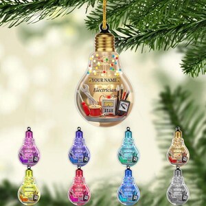 May include: A clear, lightbulb-shaped Christmas ornament with a gold cap and a gold string. The ornament has the text "YOUR NAME" and "Electrician" with tools inside. Below are 8 more ornaments in various colors.