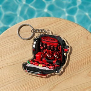 May include: A clear acrylic keychain shaped like a tool bag, featuring a black and red design with various tools. The keychain includes a silver keyring and the text "Your Name" on the top.
