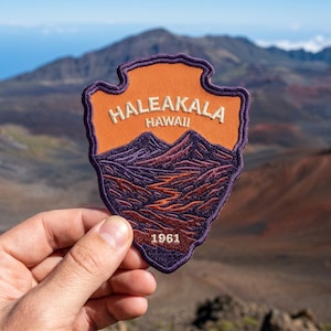 May include: A shield-shaped embroidered patch featuring an orange upper section with the text HALEAKALA HAWAII in white, and a dark purple lower section depicting a mountain landscape with the year 1961 embroidered in white at the bottom.