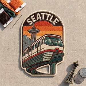 May include: An embroidered patch featuring the word SEATTLE in white text above a monorail train and the Space Needle tower. The background shows a sunset with orange and yellow horizontal stripes. The patch has a cream-colored border.