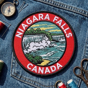 May include: A circular embroidered patch featuring a landscape of Niagara Falls with white water, green trees, and a yellow shoreline. The red border contains the white text NIAGARA FALLS and CANADA. The patch is placed on blue denim fabric.