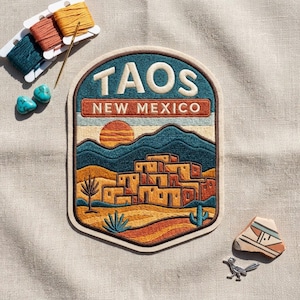 May include: An embroidered patch featuring a desert landscape with adobe buildings, mountains, and a sun. The text reads TAOS NEW MEXICO. Included are three spools of embroidery thread, a needle, two turquoise stones, and a small metal roadrunner.