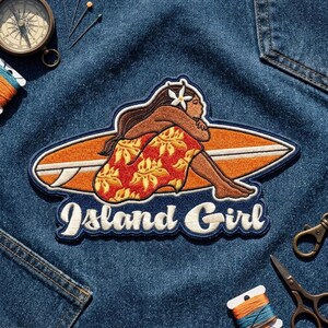 May include: An embroidered patch featuring a figure with long hair and a white flower, sitting on an orange surfboard. The patch includes the text Island Girl in white script lettering, with a dark blue border, placed on blue denim fabric.