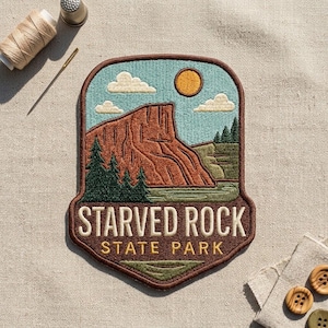 May include: An embroidered patch featuring a landscape of Starved Rock State Park with a brown rock formation, green pine trees, a yellow sun, and white clouds against a light blue sky. The text reads STARVED ROCK STATE PARK in white and yellow.