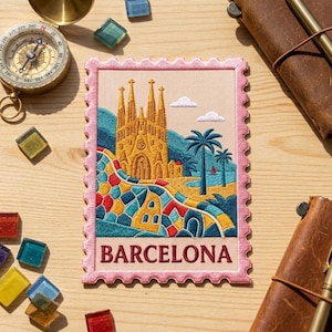 May include: A rectangular embroidered patch shaped like a postage stamp with a pink border. The design features the Sagrada Familia in gold, palm trees, and a colorful mosaic foreground. The word BARCELONA is stitched in red at the bottom.