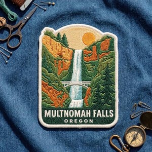 May include: A rectangular embroidered patch featuring a landscape of Multnomah Falls in Oregon. The design shows a waterfall cascading down rocky cliffs with green trees, a white bridge spanning the falls, and a yellow sun in the sky.
