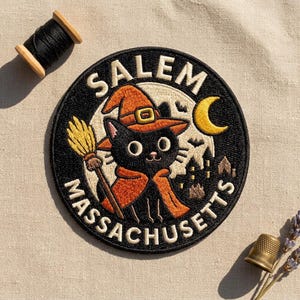 May include: A circular embroidered patch featuring a black cat wearing an orange witch hat and cape, holding a broomstick. The background shows a full moon, bats, and a silhouette of buildings. The text reads SALEM MASSACHUSETTS in cream letters.