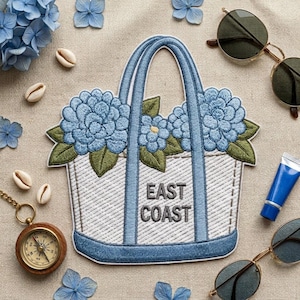 May include: An embroidered patch shaped like a white tote bag with blue trim and handles. The bag features blue hydrangea flowers with green leaves and the text EAST COAST in gray. The patch is surrounded by seashells, a compass, and sunglasses.