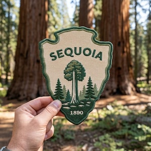 May include: A shield-shaped embroidered patch with a beige background and dark green border. It features a large central sequoia tree flanked by smaller pine trees, with the text "SEQUOIA" at the top and the number "1890" at the bottom.