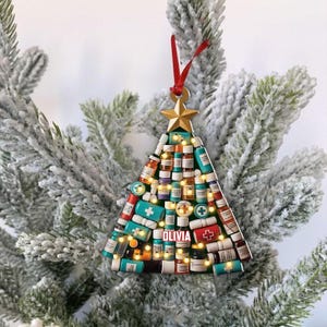 May include: A Christmas tree ornament shaped like a tree, decorated with miniature medicine bottles and a gold star. The name "Olivia" is printed on the ornament. A red ribbon is attached for hanging.