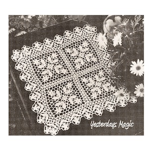 May include: A white crocheted doily with a daisy pattern. The doily is square shaped and has a scalloped edge. The doily is on a dark surface with a floral background.