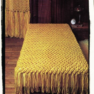 May include: A yellow crocheted throw blanket with fringe on all sides. The blanket is lying on a wooden floor.
