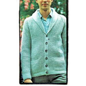 Può includere: Un uomo indossa un cardigan blu chiaro con collo a scialle e cinque bottoni. Il cardigan ha un motivo a maglia testurizzato ed è indossato sopra una camicia blu chiaro con colletto.