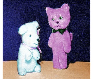 May include: A white plush dog with a pink bow and a purple plush cat with a green bow. The toys are standing on a brown surface against a dark blue background.