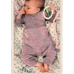 May include: A baby wearing a pink knitted onesie with a wrap-style top and holding a green and white rattle. The baby is lying on a floral patterned blanket. The word "Pixie" is written below the baby.