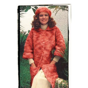 Könnte beinhalten: Eine Frau trägt einen roten Häkelmantel mit einer passenden Baskenmütze. Sie sitzt auf einer Steinmauer mit grünen Pflanzen im Hintergrund.