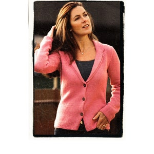 Könnte beinhalten: Eine Frau trägt einen rosa Cardigan mit V-Ausschnitt und Knopfleiste. Sie trägt darunter ein dunkles Oberteil und hat die Hand in der Tasche.