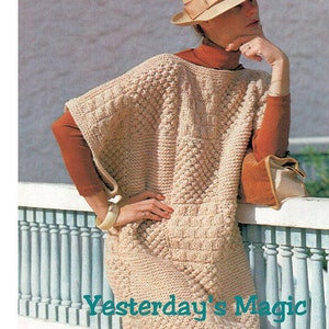 May include: A beige crocheted poncho with a textured pattern. The poncho has a wide neckline and is worn with a brown turtleneck shirt and a brown hat.
