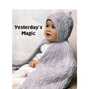 Puede incluir: Un bebé lleva una capa y un gorro con capucha de punto de color lila claro. La capa y el gorro tienen un patrón de punto de cable. El texto "Yesterday's Magic" es visible en la imagen.