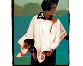 May include: A woman wearing a pink knitted poncho with a dark blue collar and a dark blue background.