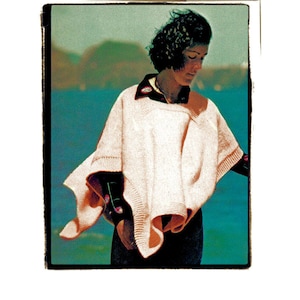 Może przedstawiać: Kobieta w różowym ponczo z dzianiny z ciemnoniebieskim kołnierzem na ciemnoniebieskim tle.