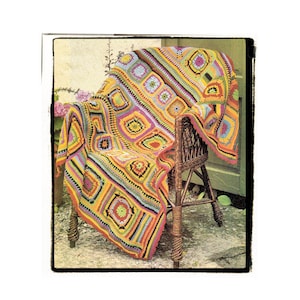 May include: A colourful crocheted throw blanket with a geometric pattern in shades of yellow, orange, green, and pink, draped over a wicker chair.