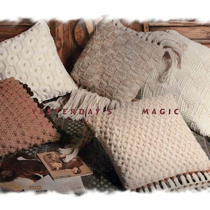 Könnte beinhalten: Fünf gestrickte Kissen in verschiedenen Texturen und Farben, darunter Beige, Braun und Weiß. Die Kissen sind auf einer Holzoberfläche mit einem gemusterten Stoff darunter angeordnet.