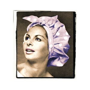 May include: A woman with blue eyes is wearing a purple and white polka dot shower cap. The cap is tied at the top with a bow.