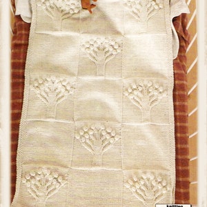 May include: A white knitted baby blanket with a repeating pattern of trees. The blanket is made with a textured yarn and has a simple, elegant design.